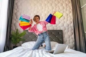 pretty happy woman jumping on bed at home shopping online photo