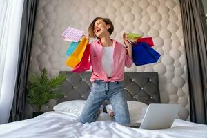 pretty happy woman jumping on bed at home shopping online photo