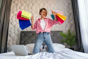 pretty happy woman jumping on bed at home shopping online photo