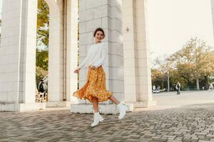 young pretty happy smiling woman in yellow printed dress and knitted white sweater photo