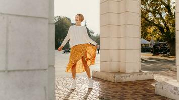 young pretty happy smiling woman in yellow printed dress and knitted white sweater photo