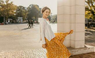 young pretty happy smiling woman in yellow printed dress and knitted white sweater photo