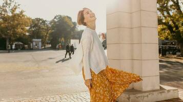 young pretty happy smiling woman in yellow printed dress and knitted white sweater photo