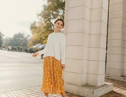 young pretty happy smiling woman in yellow printed dress and knitted white sweater photo