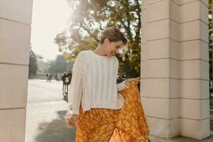 young pretty happy smiling woman in yellow printed dress and knitted white sweater photo