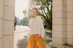 young pretty happy smiling woman in yellow printed dress and knitted white sweater photo