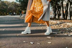 close-up legs in stylish white boots footwear of young woman in yellow printed dress photo