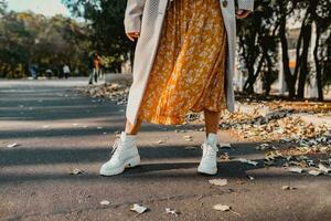 close-up legs in stylish white boots footwear of young woman in yellow printed dress photo