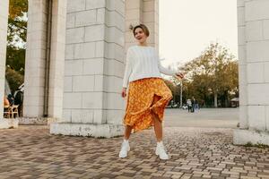 young pretty happy smiling woman in yellow printed dress and knitted white sweater photo