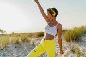 happy smiling woman listening to music in colorful yellow headphones on sunny beach in summer photo