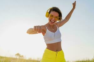 happy smiling woman listening to music in colorful yellow headphones on sunny beach in summer photo