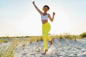 happy smiling woman listening to music in colorful yellow headphones on sunny beach in summer photo