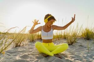 happy smiling woman listening to music in colorful yellow headphones on sunny beach in summer photo