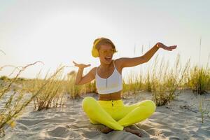 happy smiling woman listening to music in colorful yellow headphones on sunny beach in summer photo