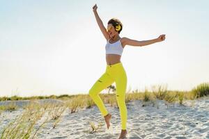 happy smiling woman listening to music in colorful yellow headphones on sunny beach in summer photo