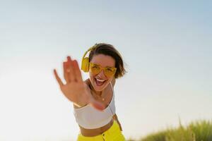 happy smiling woman listening to music in colorful yellow headphones on sunny beach in summer photo