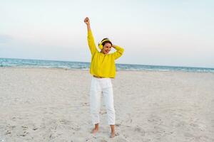 happy smiling woman listening to music in colorful yellow headphones on beach in summer photo