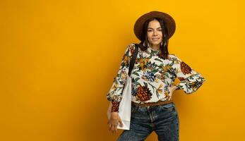 beautiful attractive stylish brunette woman posing isolated on yellow studio background in trendy fashion clothes outfit holding white shopping bag, printed blouse and hat, smiling happy, accessories photo