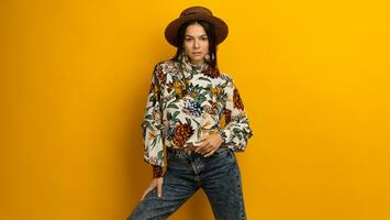 beautiful attractive stylish brunette woman posing isolated on yellow studio background in trendy fashion clothes outfit, printed blouse and hat, smiling happy, accessories photo