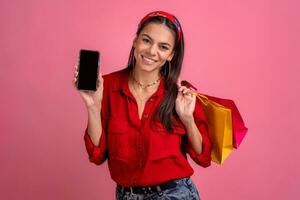 Hispano hermosa mujer en rojo camisa sonriente participación participación compras pantalones y teléfono inteligente foto