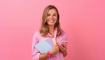 rubio bonito mujer en rosado camisa sonriente participación participación cuadernos y utilizando teléfono inteligente foto