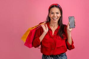 hispanic beautiful woman in red shirt smiling holding holding shopping bags and smartphone photo