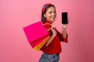 Hispano hermosa mujer en rojo camisa sonriente participación participación compras pantalones y teléfono inteligente foto