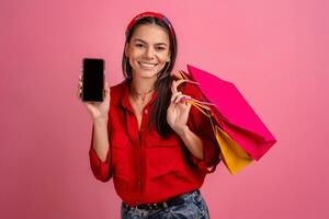 Hispano hermosa mujer en rojo camisa sonriente participación participación compras pantalones y teléfono inteligente foto