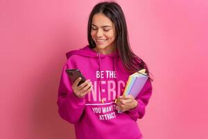 hispanic pretty woman in pink hoodie smiling holding holding notebooks and using smartphone photo