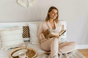 bonito sonriente mujer relajante a hogar en cama en Mañana en pijama leyendo libro foto