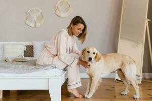 pretty smiling woman relaxing at home on bed in morning in pajamas with dog photo