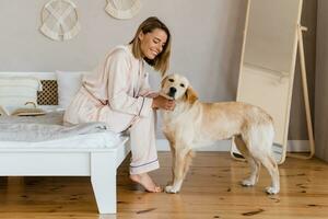 pretty smiling woman relaxing at home on bed in morning in pajamas with dog photo