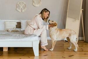 pretty smiling woman relaxing at home on bed in morning in pajamas with dog photo