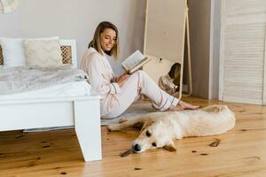 pretty smiling woman at home in morning in pajamas reading book playing with dog photo