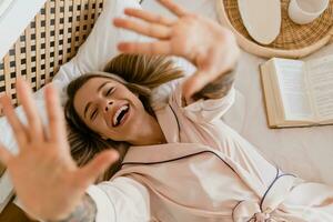 pretty smiling woman relaxing at home on bed in morning in pajamas photo