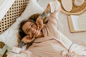 pretty smiling woman relaxing at home on bed in morning in pajamas photo