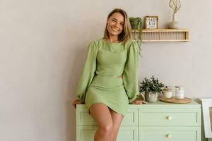 young stylish smiling woman in green summer dress in modern interior apartment home photo