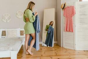 young pretty woman in green dress trying on style trend dress looking in mirror photo