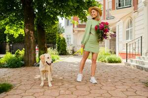 hermosa joven mujer en verano estilo atuendo sonriente contento caminando con flores y perro foto