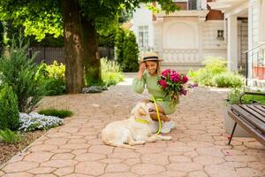 beautiful young woman in summer style outfit smiling happy walking with flowers and dog photo