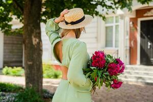 view from back on pretty young woman in summer style outfit smiling happy walking with flowers in city street photo