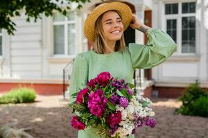 beautiful young woman in summer style outfit smiling happy walking with flowers in city street photo