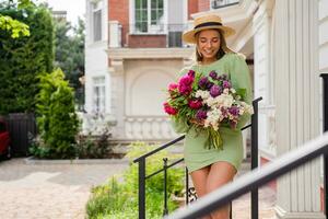 beautiful young woman in summer style outfit smiling happy walking with flowers in city street photo