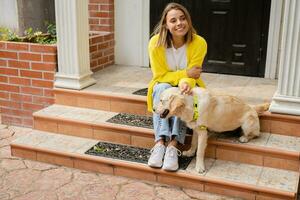 happy smiling woman in yellow sweater walking at her house with a dog golden retriever photo