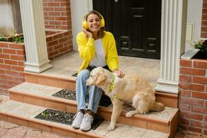 woman in yellow sweater walking at her house with a dog listening to music in headphones photo