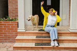 woman in yellow sweater walking at her house with a dog listening to music in headphones photo