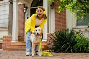 woman in yellow sweater walking at her house with a dog listening to music in headphones photo