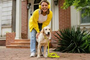 woman in yellow sweater walking at her house with a dog listening to music in headphones photo