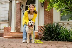 woman in yellow sweater walking at her house with a dog listening to music in headphones photo