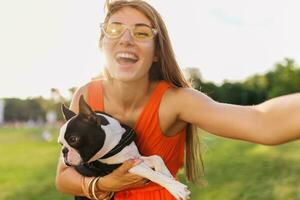 joven contento sonriente mujer en naranja vestir teniendo divertido jugando con perro en parque foto